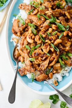 a blue plate topped with chicken and cashews on top of rice next to chopsticks