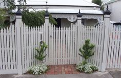 a white picket fence with potted plants on the side and brick walkway in front