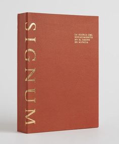 an orange book with gold lettering on the front and back cover, sitting on a white surface