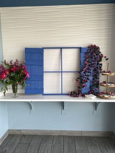 two vases with flowers are sitting on a shelf in front of a blue window