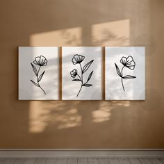 three black and white flowers are hanging on the wall in an empty room with wood flooring