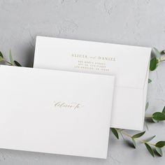 two white envelopes with gold foil lettering and greenery on the top one is open