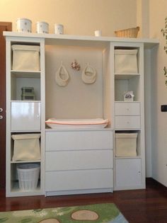 a baby changing table in the corner of a room with white cabinets and baskets on top