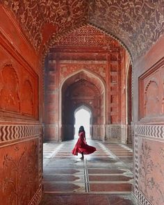 a woman in a red dress is walking through an archway