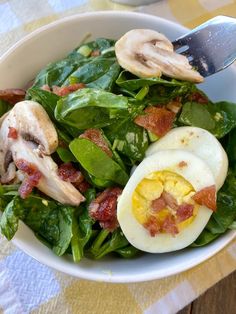 a white bowl filled with spinach and hard boiled eggs on top of bacon slices