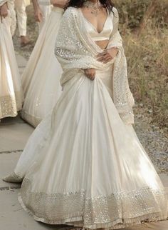 two women in white gowns walking down a path with one woman wearing a long dress