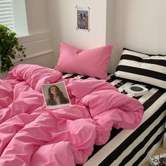 a bed covered in pink sheets and pillows next to a potted plant on the floor