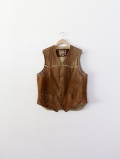 "A 1970s vintage Pioneer Wear men's shearing vest. Beautifully aged, the leather vest features warm shearling lining.  It snaps closed.  * Pioneer Wear brand * shearling vest * fur lining. * snap closure CONDITION In good condition with a nice patina and age to the leather.  MARKED SIZE: 42 MEASUREMENTS Bust:     21.5\" (43)   ...     54.6 cm (109.2) Length: 28\"           ...        71.1 cm HOW WE MEASURE → Vest measured lying flat.  → Bust measured armpit to armpit. → Length measured down the center of the back.  IC 312356" Fitted Sleeveless Rugged Outerwear, Rugged Leather Vest Outerwear, Rugged Brown Vest Outerwear, Rugged Fitted Vest Outerwear, Brown Rugged Winter Vest, Brown Rugged Vest For Winter, Rugged Brown Winter Vest, Rugged Brown Vest For Fall, Vintage Leather Vest Outerwear