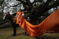 a woman in an orange dress is standing next to a horse with a long, flowing fabric draped around her