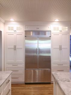 a stainless steel refrigerator in a white kitchen with wood floors and wooden flooring, along with marble countertops