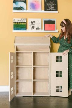 a woman holding a doll house next to a bookcase