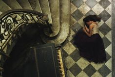 a woman sitting on the floor next to a piano in a room with checkered walls