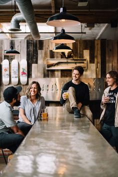 four people sitting at a bar smiling for the camera, with one person holding a drink