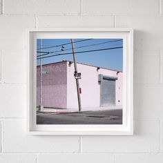 a white frame hanging on the wall above a street with pink buildings and power lines