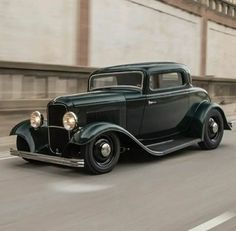 an old black car driving down the street