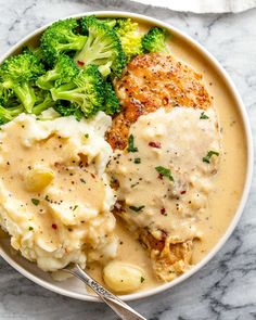 a white bowl filled with chicken, mashed potatoes and broccoli on top of a marble table