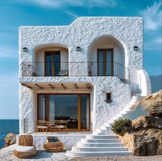 a white house with steps leading up to it and an outdoor seating area next to the ocean