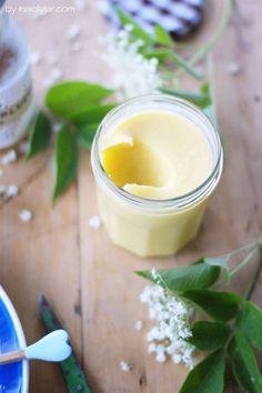 a jar filled with yellow liquid sitting on top of a wooden table next to flowers