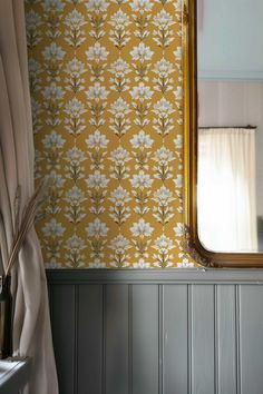 a mirror sitting on top of a wooden table next to a wallpapered wall