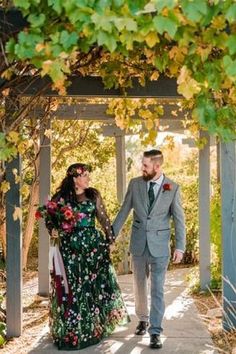 a man and woman walking down a path under an arbor with green leaves on it