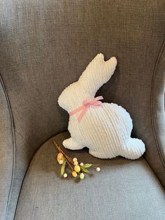 a stuffed rabbit sitting on top of a gray chair next to a branch with flowers