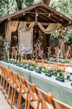 a long table with chairs and tables covered in greenery is set up for an outdoor wedding reception