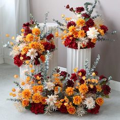 two white vases filled with red and yellow flowers next to each other on the floor