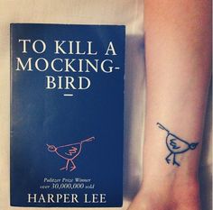 a person with a tattoo on their arm next to a book that says to kill a mocking - bird