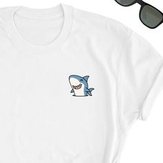 We have express delivery for our shirts! 📦⚡.  From cart to door in just 2-3 days, only for 3.5 USD extra.  You can find the express delivery option in the cart. Shark Shirt, Ocean Lover Tee Shirt, Shark Tee Top, Sharks Lover T-Shirt, Fun Shark Gift Shirt, Cute Sharks Lover Friends UNISEX Shirt Gift Friends will love it! This t-shirt feels soft and lightweight, with the right amount of stretch. It's comfortable and flattering for both men and women.  * 100% cotton (heather colors contain polyester) * Fabric weight: 5 oz  * Shoulder-to-shoulder taping * Side-seamed Time for Delivery: * Processing & production time is 1-6 business days (usually 2-3 days). * U.S. Shipping time: 3-5 business days.  * International shipping time: 4-15 days. - Please note European customers: Some orders going to Funny White Short Sleeve Top, White Crew Neck T-shirt With Cartoon Print, Funny White Crew Neck Shirt, Funny White Shirt With Cartoon Print, White Funny Shirt With Screen Print, Funny White Shirt With Screen Print, Funny White T-shirt With Screen Print, White Funny T-shirt, White Shirt With Funny Print