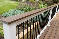 a wooden deck with white railing and black handrails in front of green grass