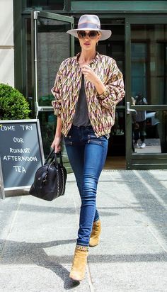 a woman walking down the street while wearing a hat and carrying a handbag in her right hand