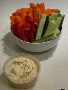 a white bowl filled with cucumbers and carrots next to a container of dip