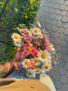 a vase filled with lots of flowers sitting on top of a person's lap