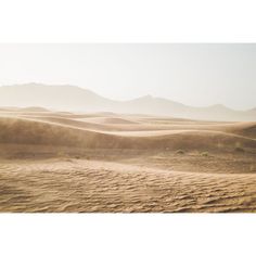 sand dunes in the desert with mountains in the backgrouds and dust blowing from them