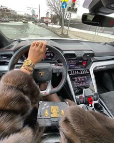 a woman driving a car with her hands on the steering wheel and wearing a fur coat