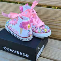 a pair of shoes with pink bows are on top of a box that is sitting on a wooden bench