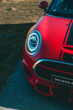 the front end of a red sports car parked in a parking lot next to grass