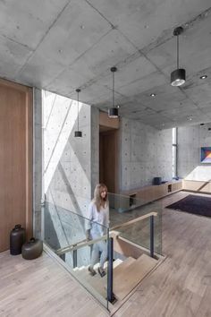 a woman walking up some stairs in a room with concrete walls and floor to ceiling windows