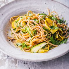 a white bowl filled with noodles, zucchini and squash on top of a wooden table