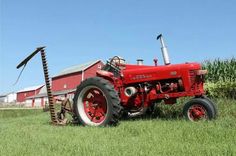 an old red tractor parked in the middle of a field