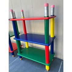 three tiered toy shelf with colorful paint on the top and bottom, in front of a white wall