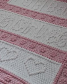 a pink and white crocheted blanket with hearts on it