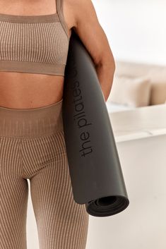 a woman holding a yoga mat in her right hand and wearing leggings with no bra