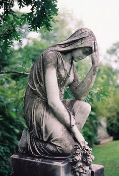 a statue of a woman sitting on top of a cement block in the grass with her hands to her face