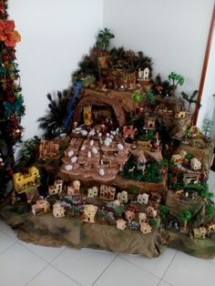 there are many small toy houses on the rocks in front of the christmas tree that is decorated