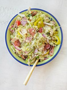 a salad in a green and blue bowl with a wooden serving utensil next to it