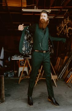 a man with a beard in a green suit and black shoes is holding his arms out