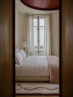 a bed sitting under a window in a bedroom next to a tall wooden frame with two lamps on top of it