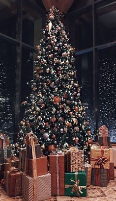 a christmas tree with presents under it in front of a large glass window at night