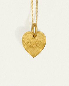 Graced with eagle reliefs on both sides, this solid gold heart necklace embodies bravery and love. The design draws inspiration from the Latin word for heart, originally signifying the courageous expression of one's true feelings.  
 Crafted from 24k solid gold, this double-sided pendant exudes a rich, tactile lustre that enhances its allure. A 14k yellow gold curb chain completes the Courage Necklace. Tarnish Resistant Yellow Gold Heart Pendant Necklace, Brass Heart Charm Medallion Jewelry, Heart-shaped Yellow Gold Brass Necklace, Yellow Gold Heart-shaped Brass Necklace, Heart Shaped Yellow Gold Brass Necklace, Symbolic Gold Heart-shaped Necklaces, Engraved Double Heart Yellow Gold Jewelry, Yellow Gold Brass Necklace With Heart Charm, Engraved Brass Heart Pendant Jewelry